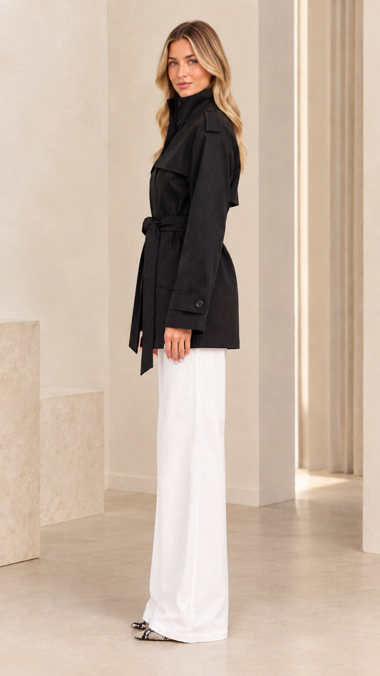 Side view of model wearing black belted short trench coat with stand collar