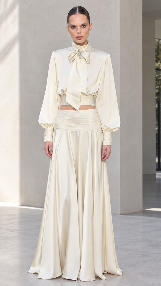 Front view of model wearing ivory satin bow tie blouse and matching pleated maxi skirt set