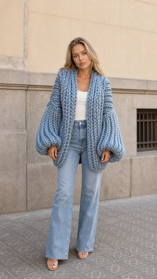 Front view of woman wearing slate blue chunky knit cardigan with balloon sleeves and light wash jeans